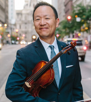 David Kim standing in the street holding a violin