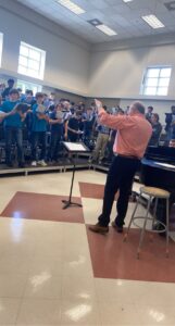 A conductor leads high school students in song