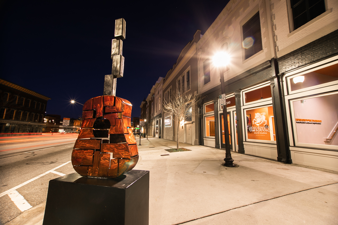 A night street view of Capricorn Music's building in the back, with a guitar sculpture in the foreground