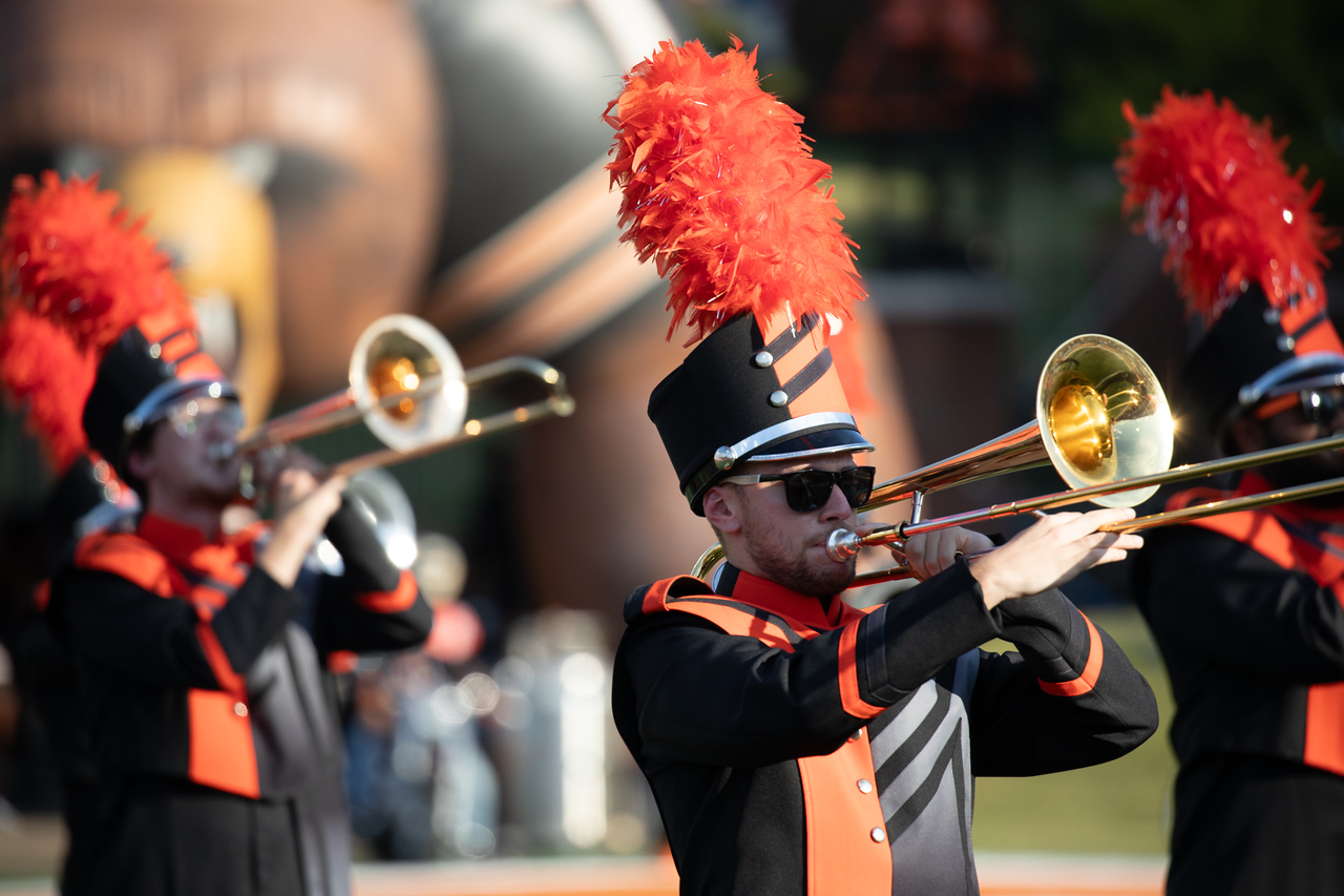 Marching band members in uniform on the football field playing trombone