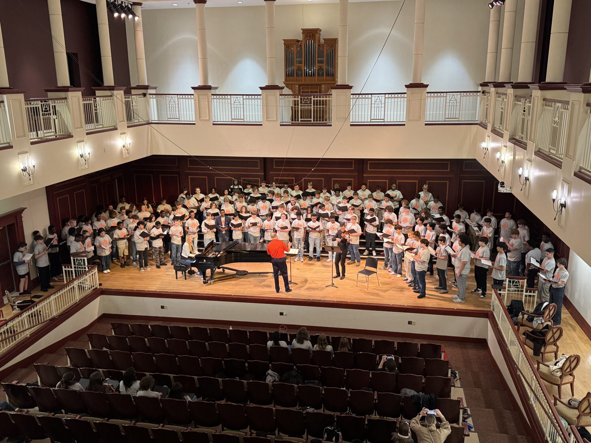 175 tenor and bass singers on stage with a piano, violinist, and conductor