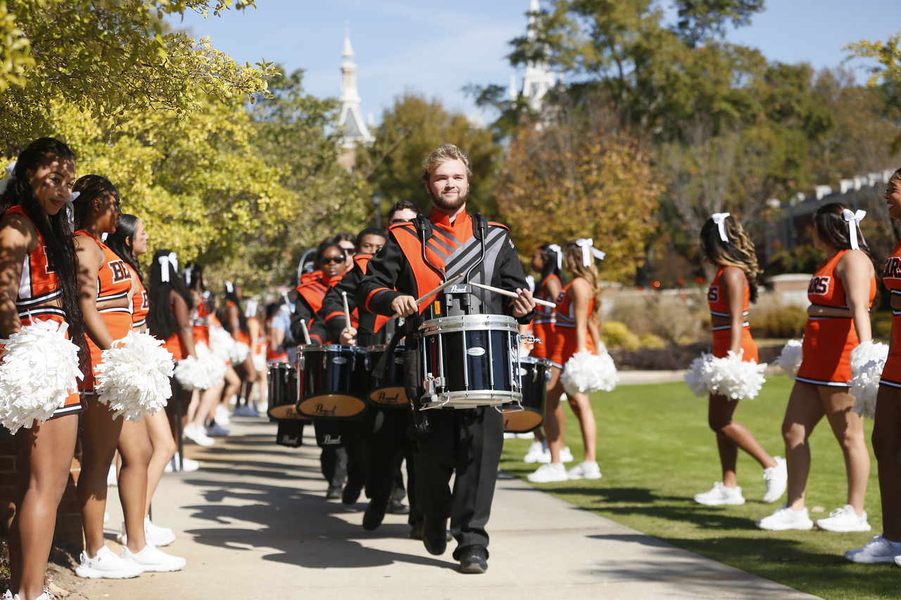 A percussion member of the marching band leads a procession of band members